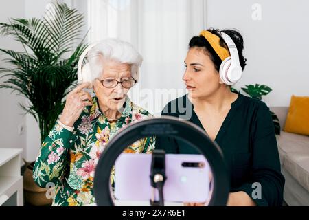 Une femme âgée et une jeune femme adulte sont assis ensemble pour enregistrer un podcast. Ils portent tous les deux des écouteurs et parlent dans un microphone, enregistrant avec un sma Banque D'Images