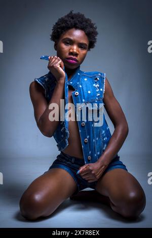 Une jeune femme africaine confiante avec des cheveux naturels, berçant un élégant gilet en denim à motif étoiles. Portraits tendance et cool de mode studio. Banque D'Images