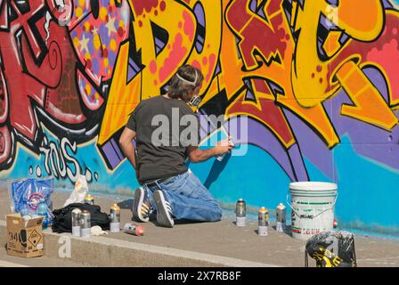 Artiste graffiti masculin utilisant le spray pour une grande murale Banque D'Images