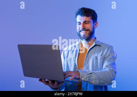 Homme sourit en utilisant un ordinateur portable dans la lumière néon Banque D'Images