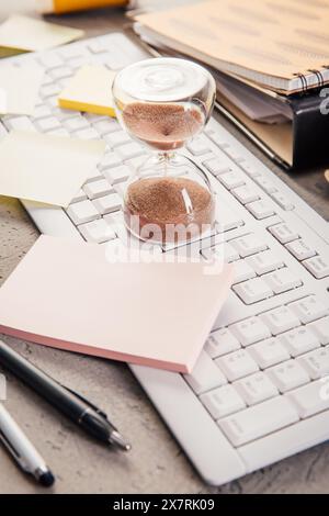 Récolte du sablier sur la table de bureau à domicile compter le temps de mesure. Lieu de travail de l'employé occupé, la gestion du temps et le concept d'épuisement professionnel Banque D'Images