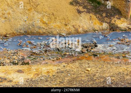 Rivière de source chaude minérale bleue entourée de sol de soufre orange et de pierres dans la zone géothermique de Seltun à Krysuvik, Islande. Banque D'Images