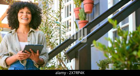 Portrait de jeune femme adulte souriante avec tablette numérique travaillant dans le centre de jardinage vérifiant les plantes Banque D'Images
