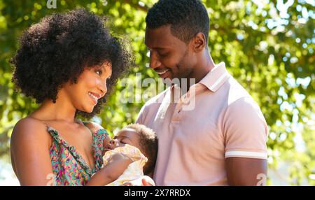 Parents amoureux Cuddling bébé dormir fille à l'extérieur dans le jardin ou la campagne ensemble Banque D'Images