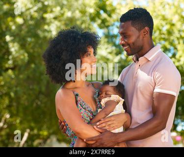 Parents amoureux Cuddling bébé dormir fille à l'extérieur dans le jardin ou la campagne ensemble Banque D'Images