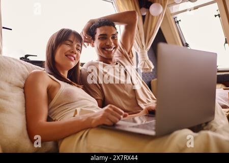 Un homme et une femme se détendent sur un lit, plongés dans un écran d'ordinateur portable, reflétant une façon moderne de se lier dans un cadre intime. Banque D'Images