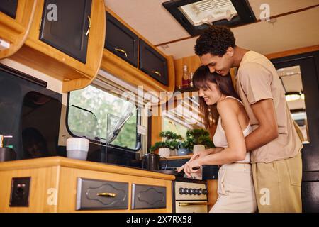 Un couple interracial se tient ensemble dans une cuisine cosy, partageant un moment d’intimité et de partenariat tout en préparant un repas. Banque D'Images