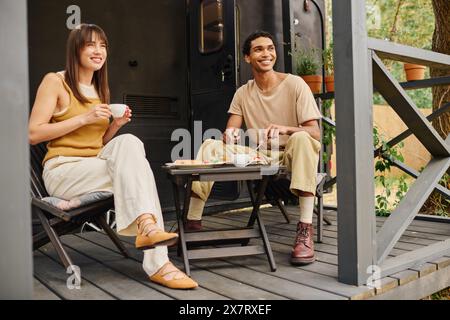 Un couple interracial se détend ensemble sur un porche confortable, appréciant les uns les autres compagnie dans un cadre paisible. Banque D'Images