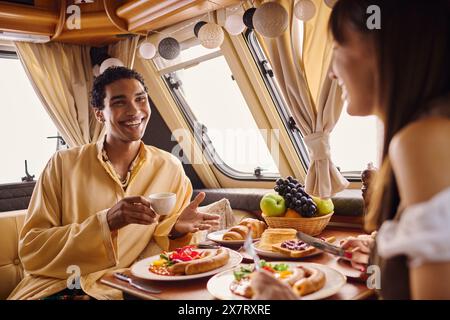 Un couple interracial profite d'un délicieux repas ensemble dans un camping-car, créant des souvenirs lors d'une escapade romantique. Banque D'Images