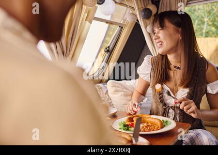Une femme d'ethnie diverse assise dans un bus, savourant une assiette de nourriture. Banque D'Images