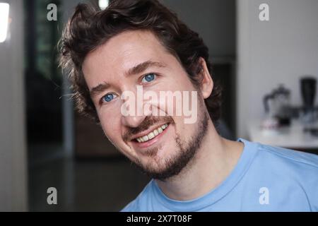 Beau jeune homme aux yeux bleus et aux cheveux ondulés souriants Banque D'Images