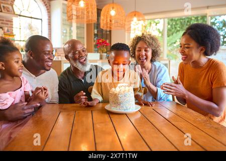 Famille multi-génération célébrant l'anniversaire de son petit-fils à la maison soufflant des bougies sur un gâteau Banque D'Images