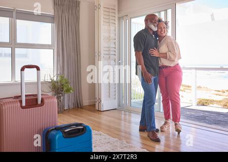 Couple d'âge mûr aimant avec bagages arrivant à Beachfront House surplombant l'océan pour des vacances d'été Banque D'Images