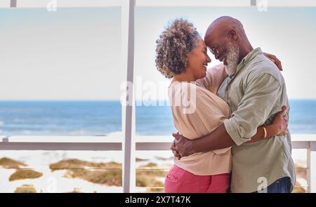 Couple d'âge mûr amoureux embrassant dans Beachfront House surplombant l'océan pour des vacances d'été Banque D'Images