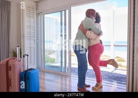 Couple d'âge mûr aimant avec bagages arrivant à Beachfront House surplombant l'océan pour des vacances d'été Banque D'Images