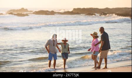 Couple d'âge mûr avec des amis en vacances marchant à travers les vagues sur Beach Shoreline au coucher du soleil Banque D'Images