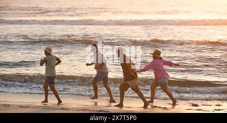 Couple d'âge mûr avec des amis en vacances marchant à travers les vagues sur Beach Shoreline au coucher du soleil Banque D'Images
