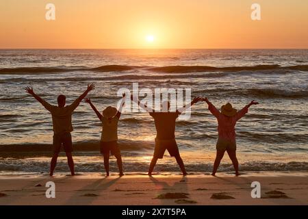 Silhouette de couples d'âge mûr sur la plage regardant vers la mer au coucher du soleil avec les bras tendus Banque D'Images