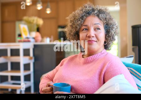 Femme mature assise sur le canapé à la maison se relaxant avec une boisson chaude Banque D'Images