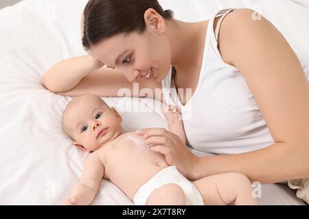 Jeune femme heureuse appliquant la crème pour le corps sur la peau du bébé sur le lit Banque D'Images