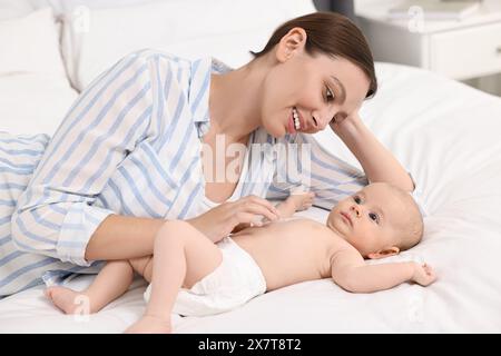 Jeune femme heureuse appliquant la crème pour le corps sur la peau du bébé sur le lit Banque D'Images