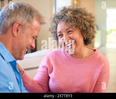 Amoureux couple mature multi-racial assis sur un canapé à la maison rire et parler ensemble Banque D'Images