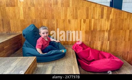 enfant mignon ayant assis sur le sac de haricots gris près de l'autre chaise de sac rouge Banque D'Images