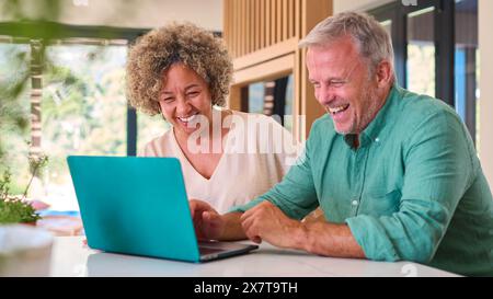 Couple mature multi-racial souriant à la maison regardant l'ordinateur portable ensemble Banque D'Images