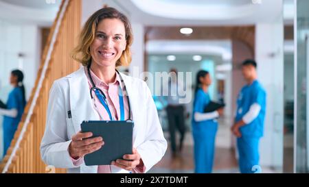 Portrait de femme médecin en manteau blanc et tablette numérique à l'hôpital avec des collègues en arrière-plan Banque D'Images