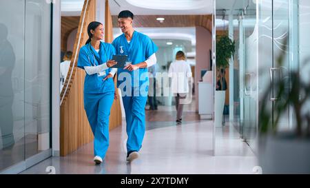 Hommes et femmes médecins ou infirmières dans les gommages avec tablette numérique à l'hôpital avec des collègues derrière Banque D'Images