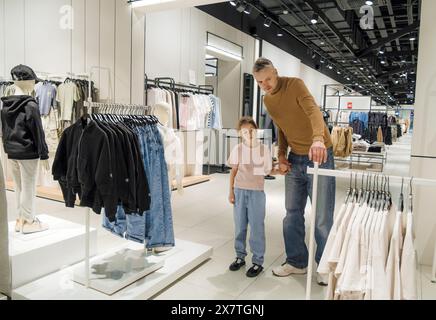 Un homme et une petite fille sont debout devant un porte-vêtements. Banque D'Images