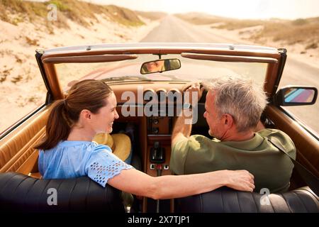 Couple senior retraité en vacances conduisant en voiture de sport classique sur la route à travers la campagne Banque D'Images