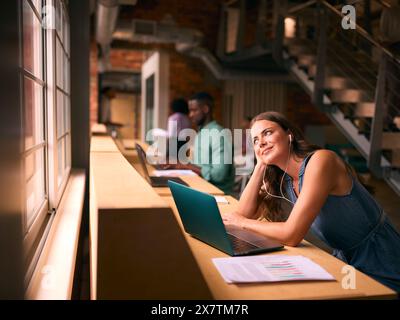 Femme d'affaires travaillant dans le bureau multiculturel moderne écoutant de la musique sur des écouteurs ou des écouteurs Banque D'Images