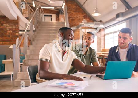 Trois hommes d'affaires se réunissant dans le bureau moderne assis autour de la table travaillant sur l'ordinateur portable ensemble Banque D'Images