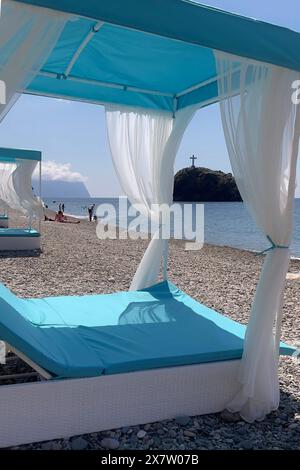 Un parasol bleu et blanc avec des rideaux blancs est installé sur une plage Banque D'Images