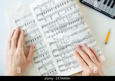 Les mains d une personne sont vues sur une feuille de musique avec un crayon et un clavier en arrière-plan Banque D'Images