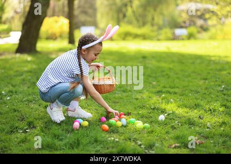 Fête de Pâques. Petite fille mignonne dans les oreilles de lapin chassant les œufs à l'extérieur, espace pour le texte Banque D'Images