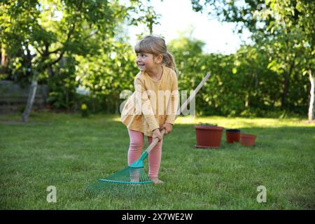 Mignonne petite fille avec râteau dans le jardin le jour de printemps Banque D'Images