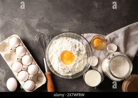 Faire de la pâte. Farine avec jaune d'oeuf dans un bol et d'autres produits sur une table texturée grise, pose à plat Banque D'Images