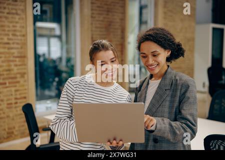 Deux collègues féminines occupées discutant du projet debout dans le bureau avec un ordinateur portable Banque D'Images
