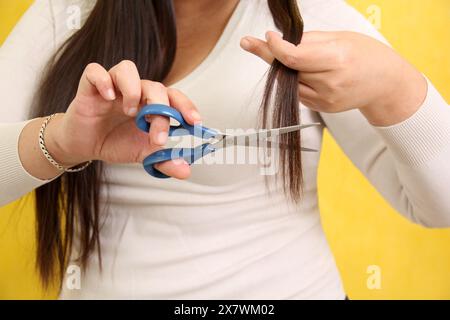 Une femme Latina de 40 ans souffre de cheveux abîmés et coupe les pointes fourchues avec des ciseaux, désespérée pour les dommages Banque D'Images