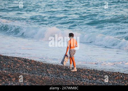 Nice, France - 29.09.2022 : Un jeune homme marche le long de la plage à la lumière du soleil couchant Banque D'Images