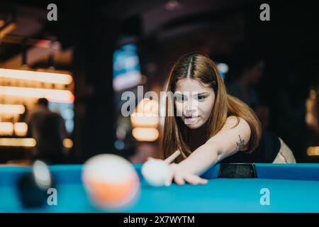 Jeune femme jouissant d'une partie de billard, axée sur la stratégie et le plaisir avec des amis dans un bar animé Banque D'Images