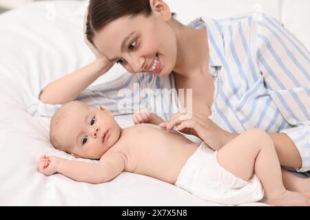 Jeune femme heureuse appliquant la crème pour le corps sur la peau du bébé sur le lit Banque D'Images