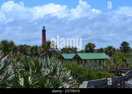 Le phare de Ponce Inlet se dresse au loin derrière les dunes, avec deux pavillons nichés dans le feuillage sous un ciel bleu nuageux en Floride. Banque D'Images