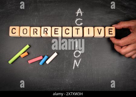 Action corrective. Puzzle de mots croisés en bloc en bois et morceaux de craie sur un fond de tableau noir. Banque D'Images