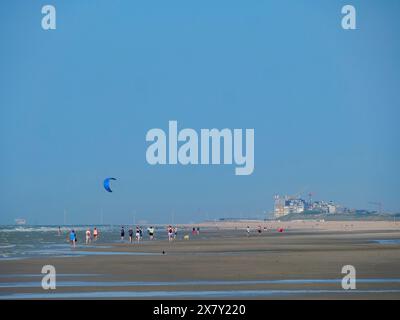 Les gens marchant le long de la plage, un kitesurfer en arrière-plan, une large plage de sable au bord de la mer avec des mouettes et un panorama de la ville sur la promenade, de haa Banque D'Images