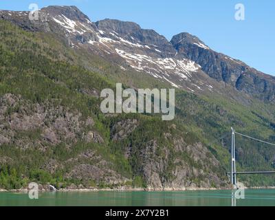 Hautes montagnes avec des restes de neige sur les sommets, des pentes boisées verdoyantes et un grand pont sous un ciel clair, pont dans un fjord avec mou enneigé Banque D'Images