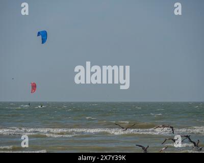 Deux cerfs-volants colorés planant dans le ciel bleu au-dessus de quelques oiseaux et les vagues sur la plage, large plage de sable au bord de la mer avec des mouettes et un panorama de la ville Banque D'Images