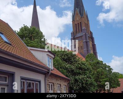 Église avec haute tour dans un petit village, entourée d'arbres verts et de nuages blancs dans le ciel bleu, grandes tours d'église avec des arbres et hou historique Banque D'Images